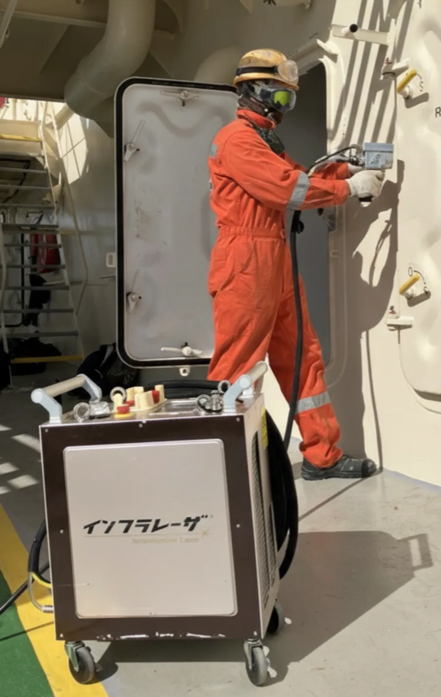 船内の扉まわりでレーザ施工を行う作業者と、離れた位置に置かれたインフラレーザ®本体
